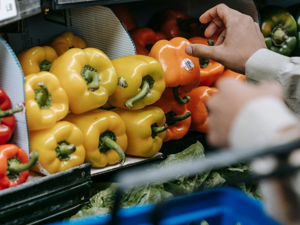 Crop unrecognizable buyer choosing ripe colorful bell peppers while standing in department with fresh vegetables during grocery shopping in supermarket